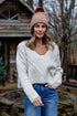 Woman wearing a white sweater, blue jeans, and a pink beanie outdoors.
