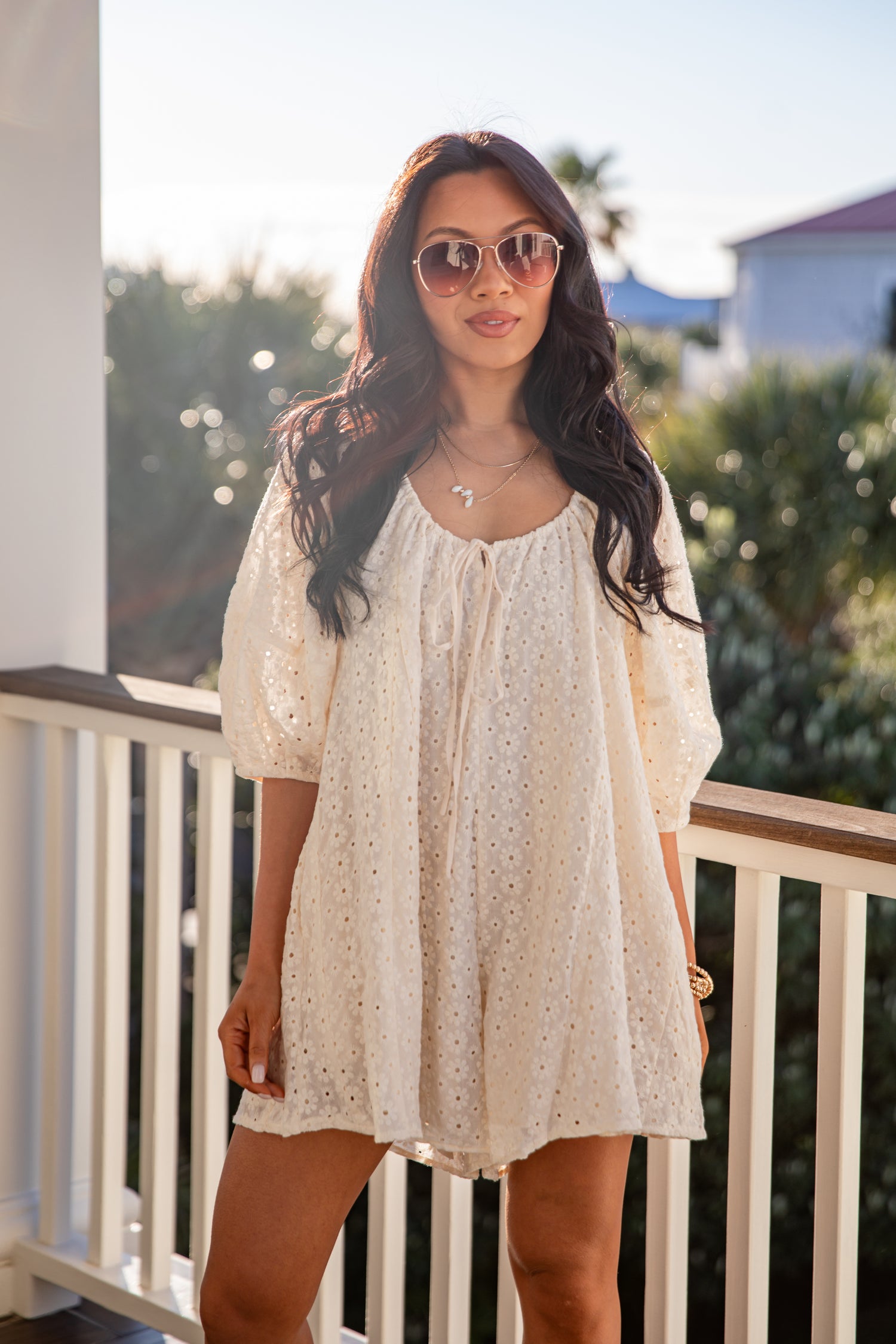 Woman wearing a white lace dress on a balcony with a blurred outdoor background