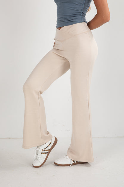 Person wearing beige flared pants and white sneakers on a plain background