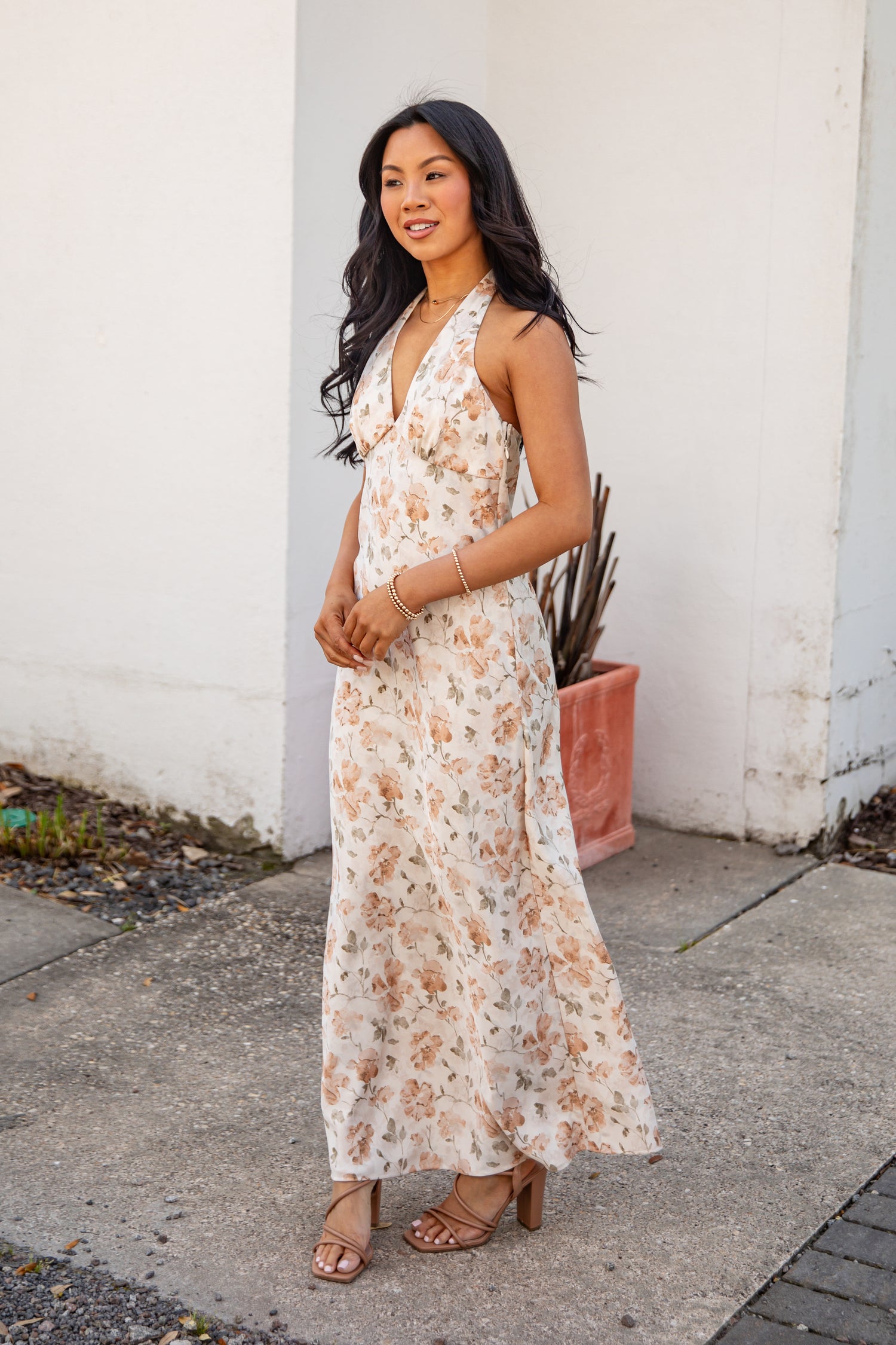 Woman in a floral dress standing against a white wall.