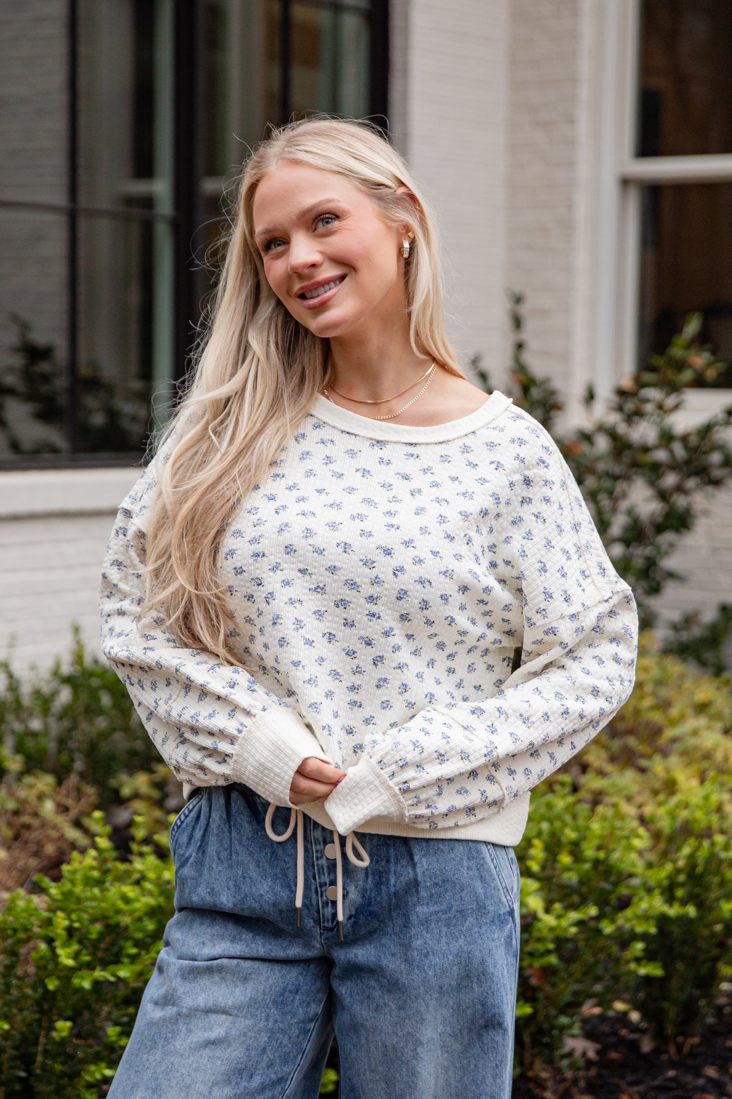 Woman wearing a white patterned sweater and blue jeans standing outdoors.