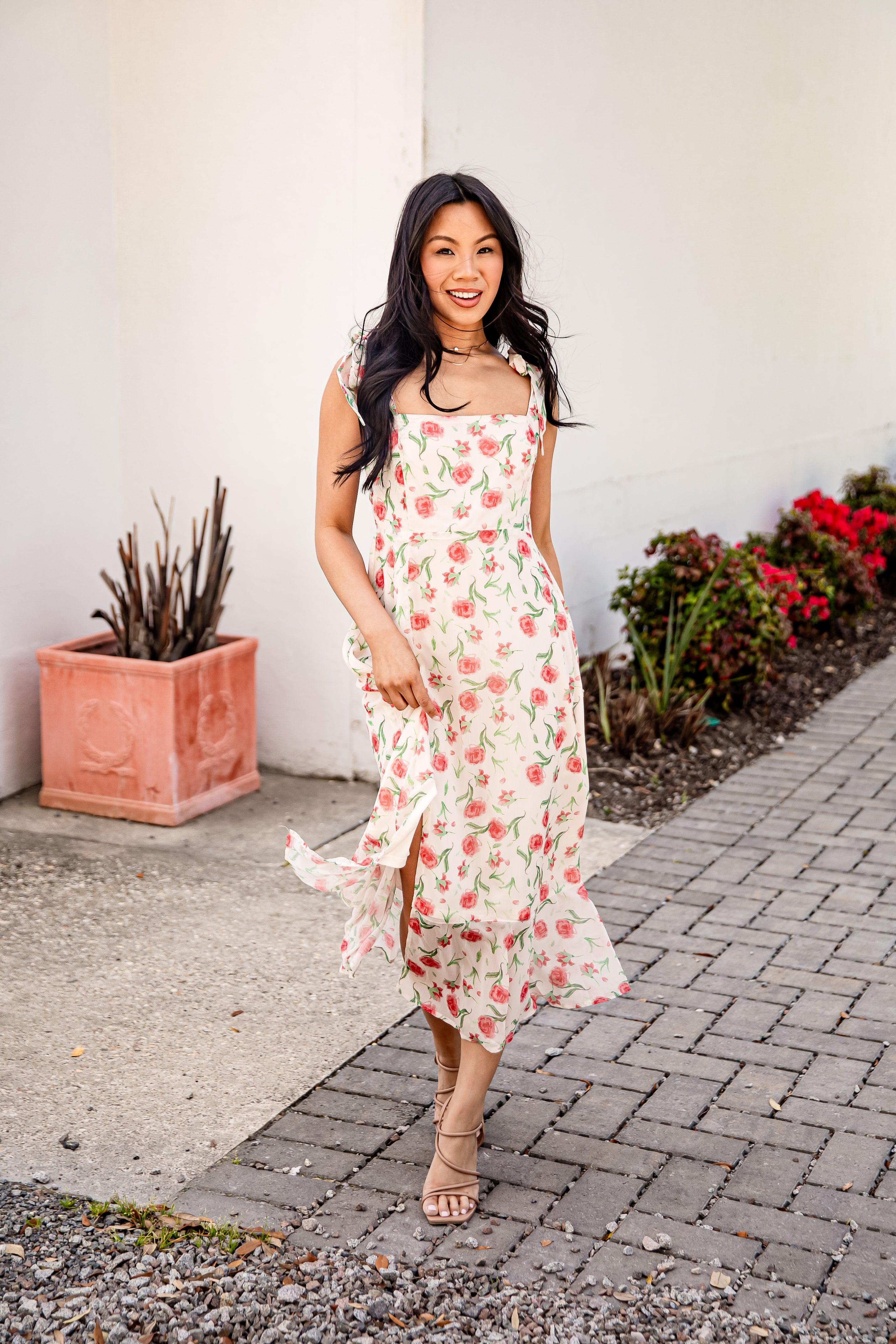 Woman in a floral dress standing on a sidewalk with plants in the background