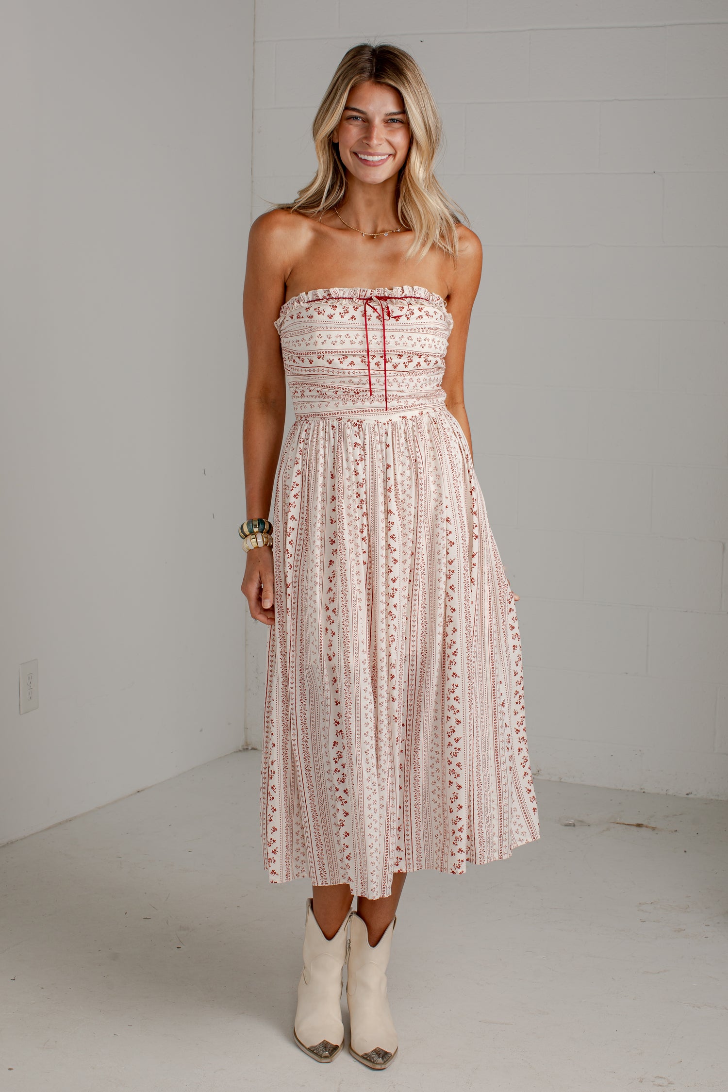 A woman modeling a strapless midi dress with a pink and white bohemian pattern, standing in a white studio setting.