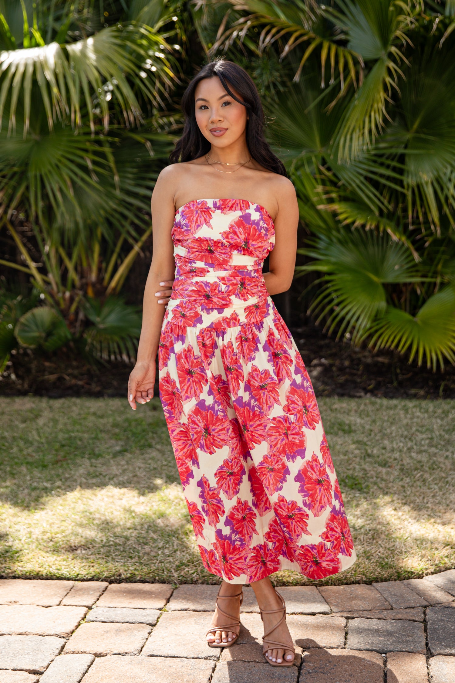 Woman wearing a strapless floral dress standing outdoors with greenery in the background