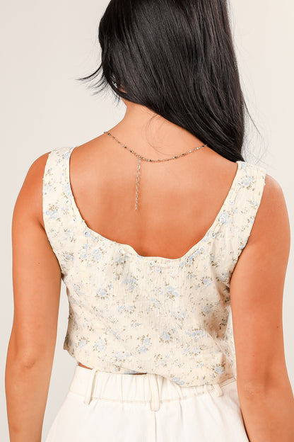Back view of a person wearing a floral sleeveless top on a plain background