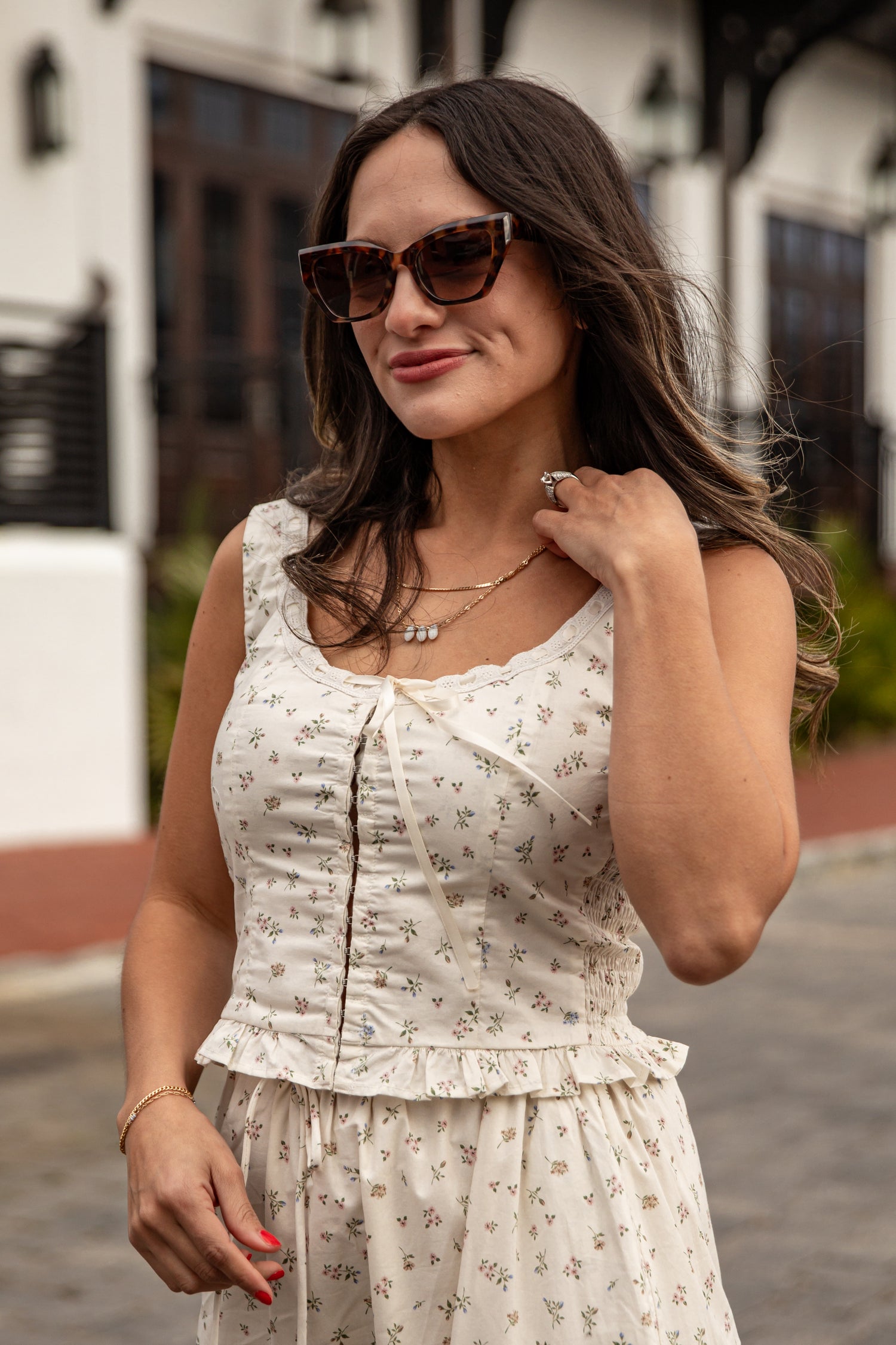 Woman wearing a white floral dress and sunglasses outdoors.