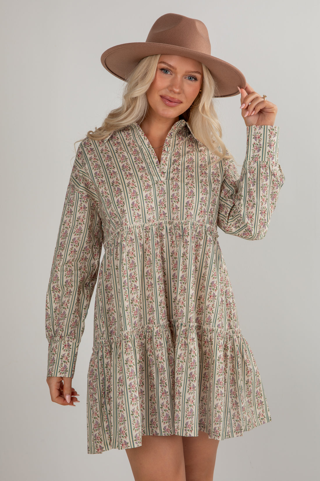 Woman wearing a patterned dress and brown hat on a plain background