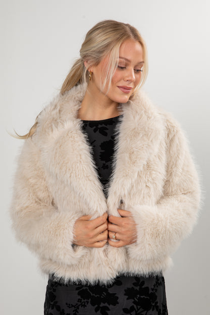Woman wearing a beige fur coat against a white background