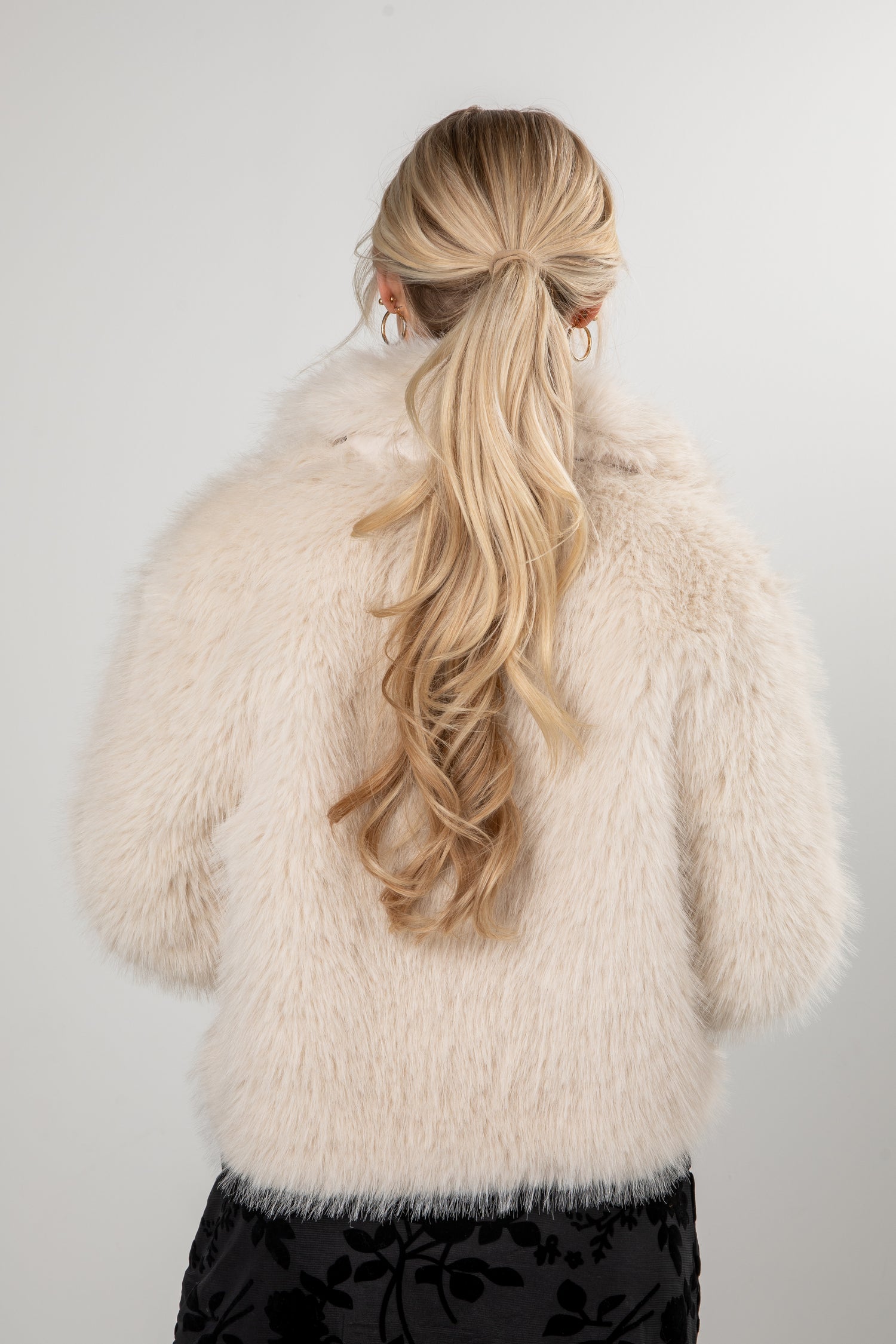 Person wearing a fluffy white coat with long blonde hair styled in a ponytail against a plain background