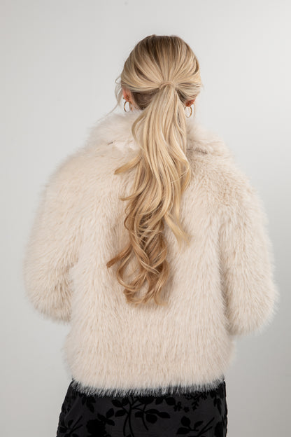 Person wearing a fluffy white coat with long blonde hair styled in a ponytail against a plain background