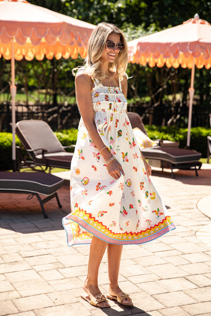 Woman in a colorful dress standing on a patio with umbrellas and lounge chairs.