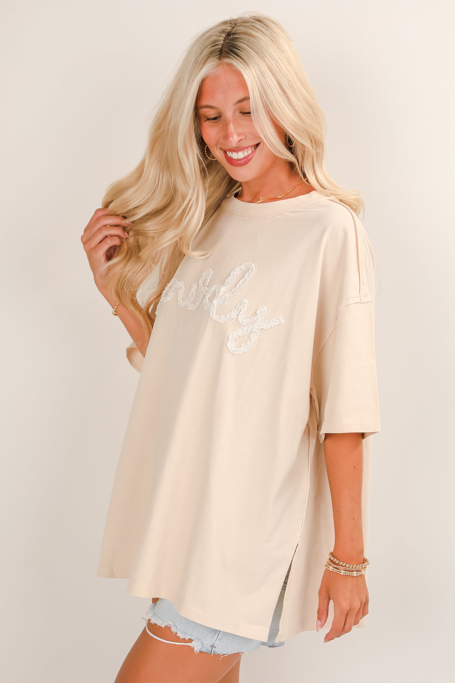 Woman wearing a beige oversized t-shirt with text on a plain background
