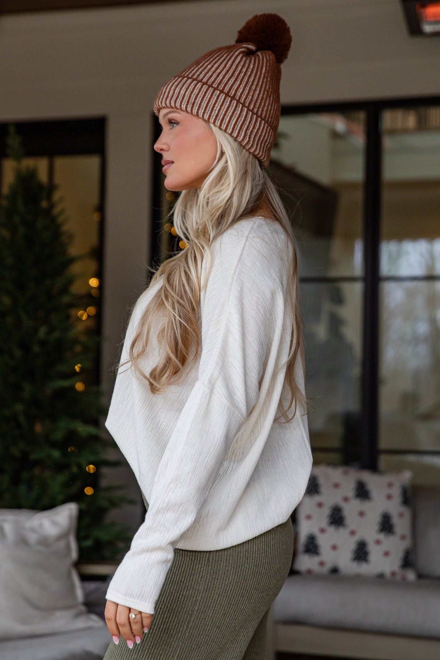 Woman wearing a white sweater and brown beanie in a cozy indoor setting.