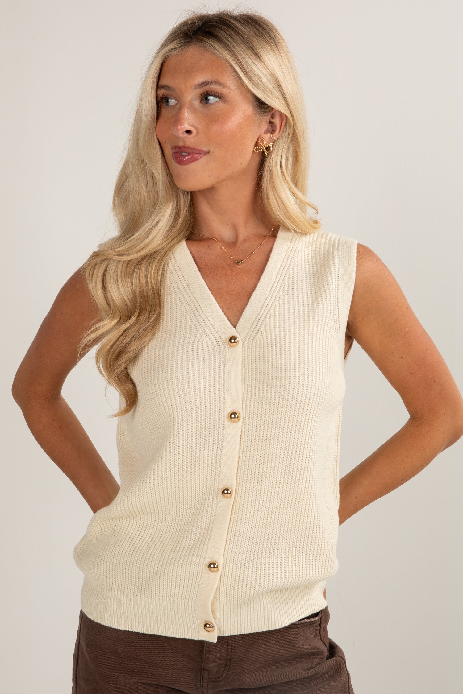 Woman wearing a beige sleeveless cardigan against a plain background