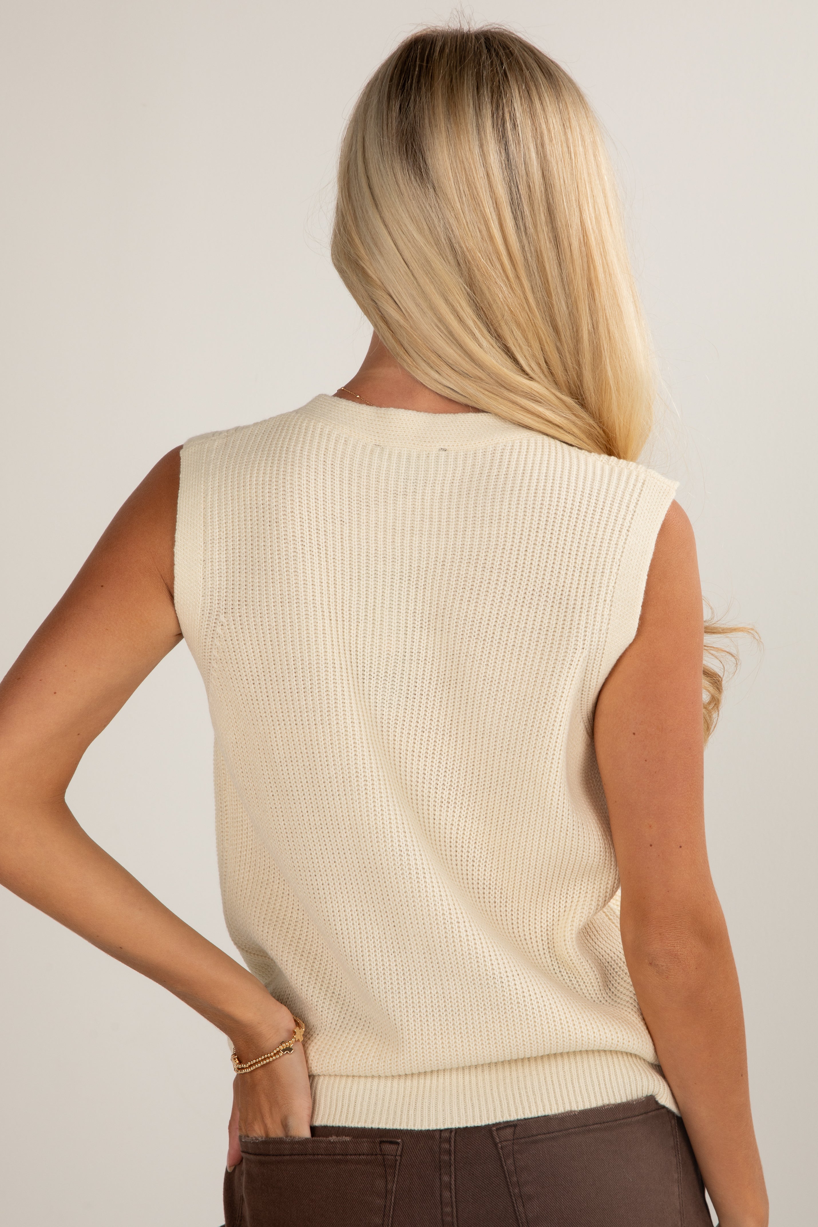 Woman wearing a beige sleeveless sweater against a plain background
