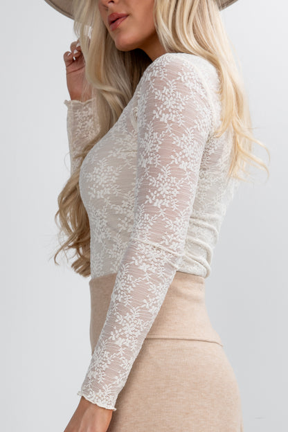 Person wearing a white lace long-sleeve top and beige pants on a plain background