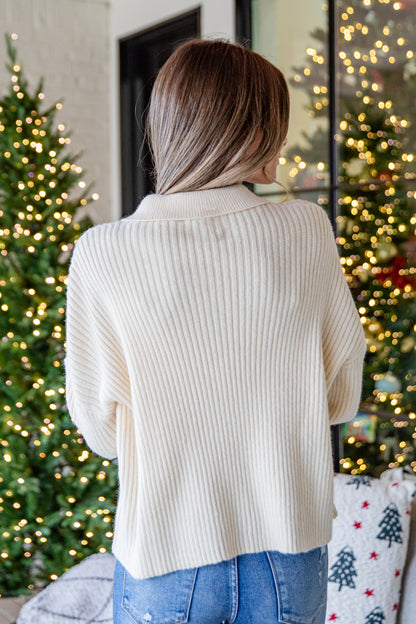 Woman wearing a beige sweater in front of Christmas trees