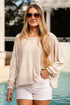 Woman in a beige top and white shorts standing by a pool.