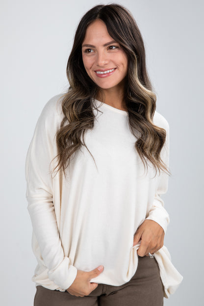 Woman wearing a white long-sleeve top against a plain background