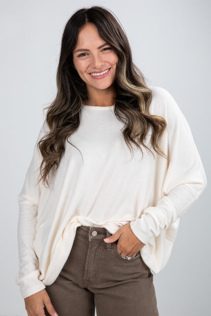 Woman wearing a white sweater and brown pants against a plain background