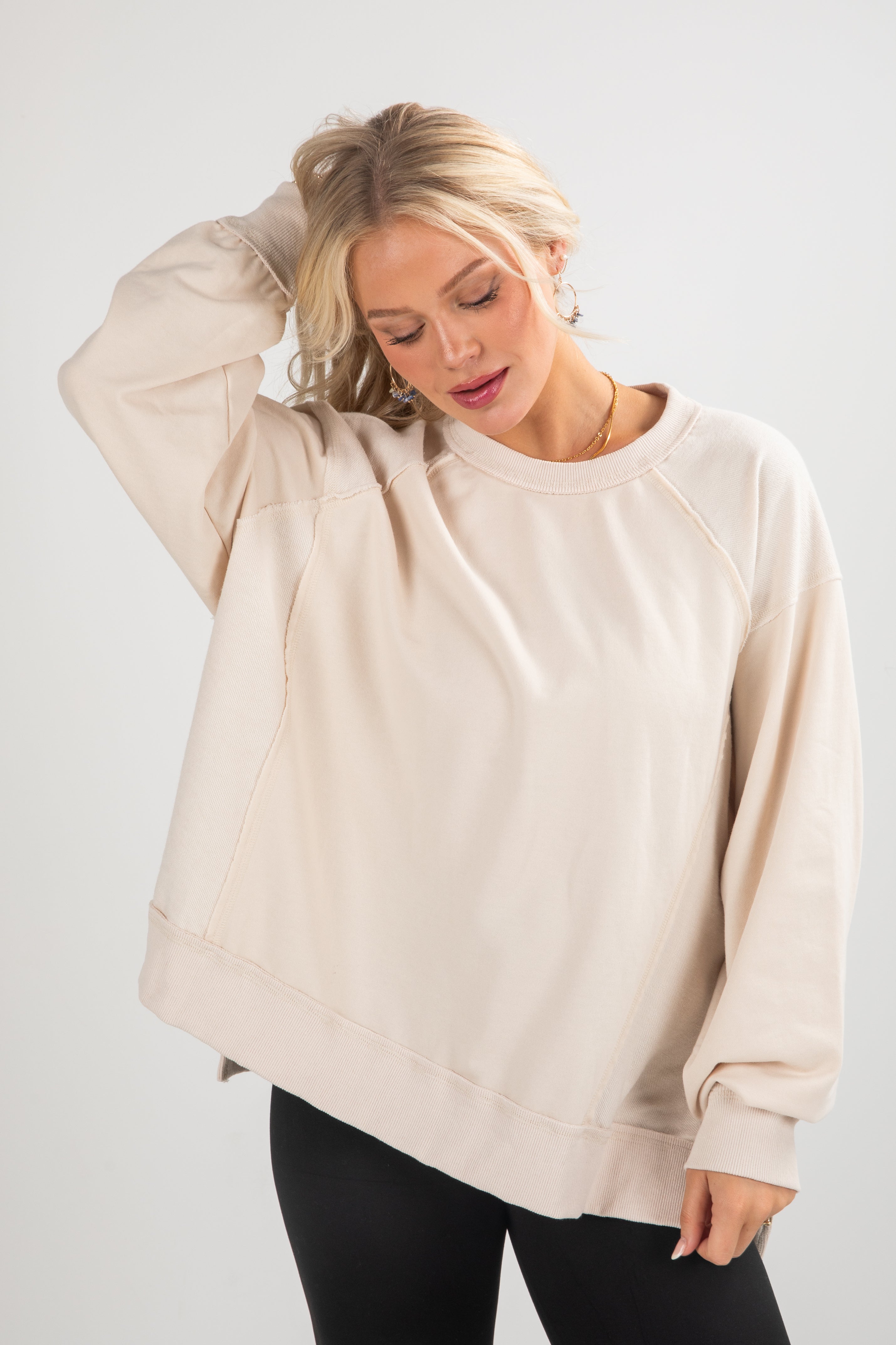 Woman wearing a beige oversized sweatshirt against a white background