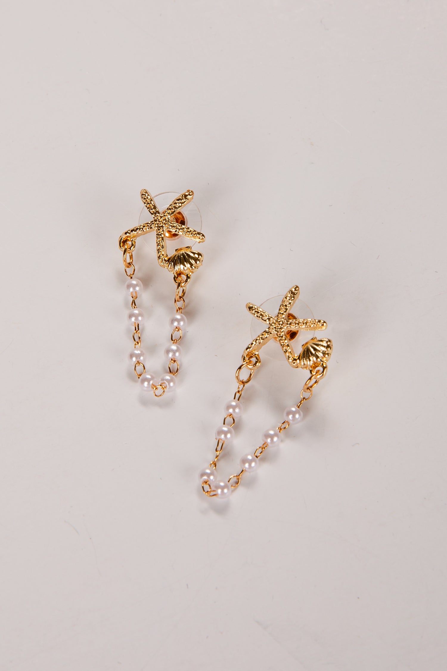 Gold starfish earrings with pearl-like beads on a light gray background