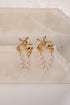 Gold starfish earrings with pearl chains on a beige stone surface
