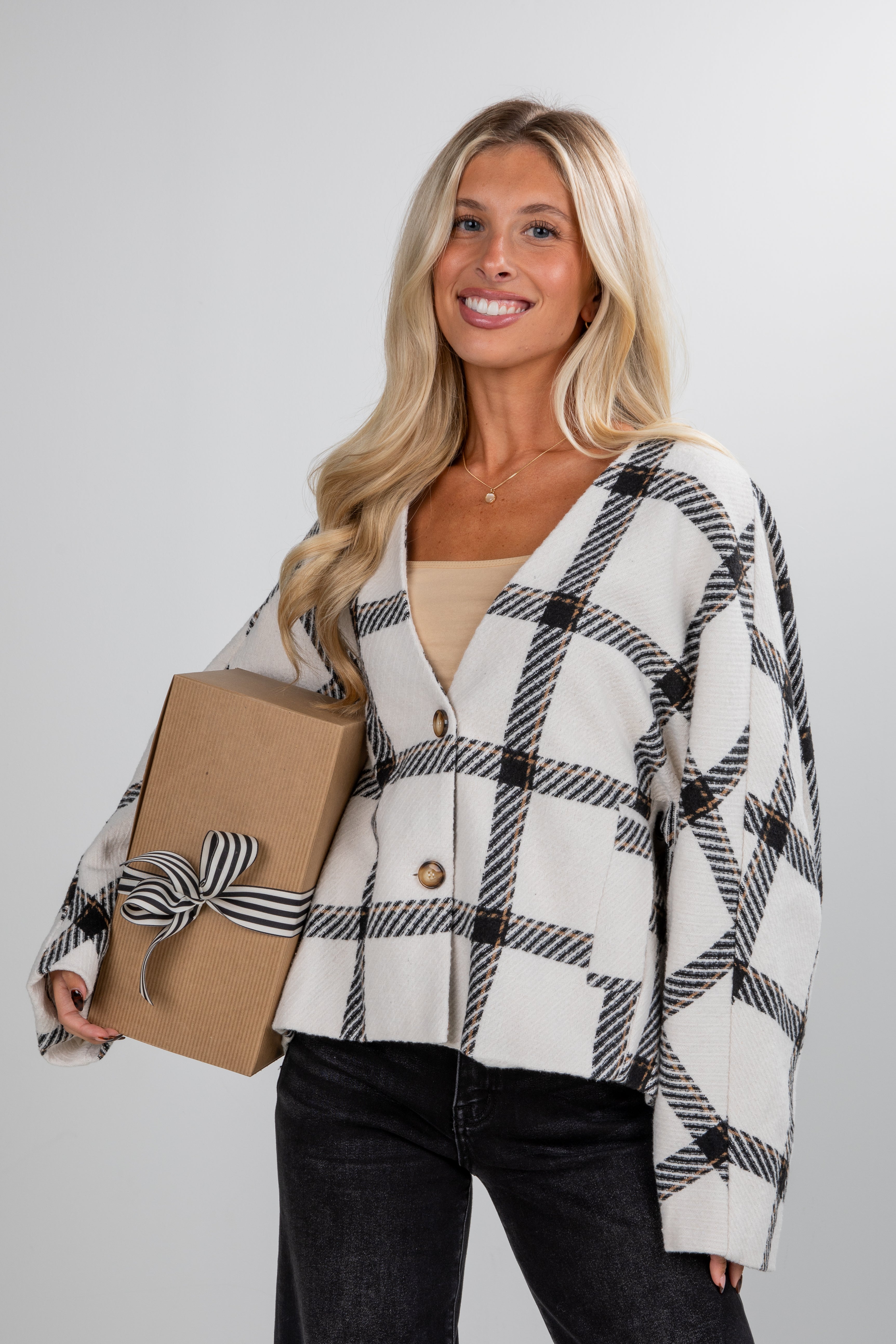 Woman wearing a plaid cardigan holding a gift box against a plain background
