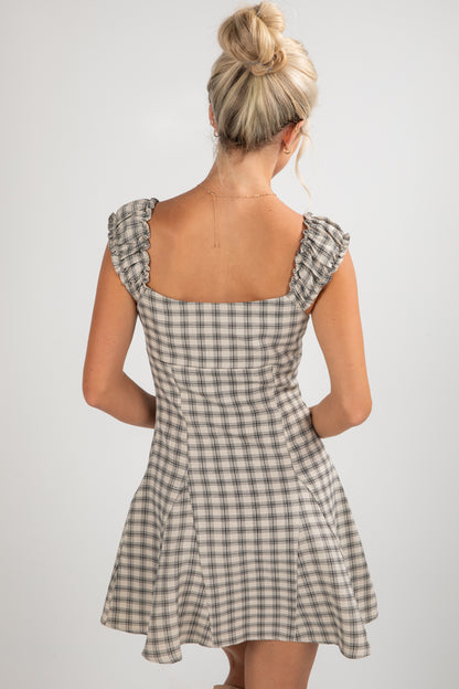 Woman wearing a checkered dress with ruffled shoulders on a plain background