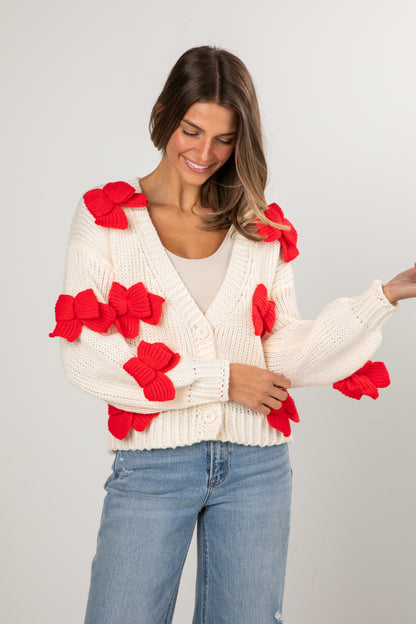 Woman wearing a white sweater with red floral patterns on a plain background