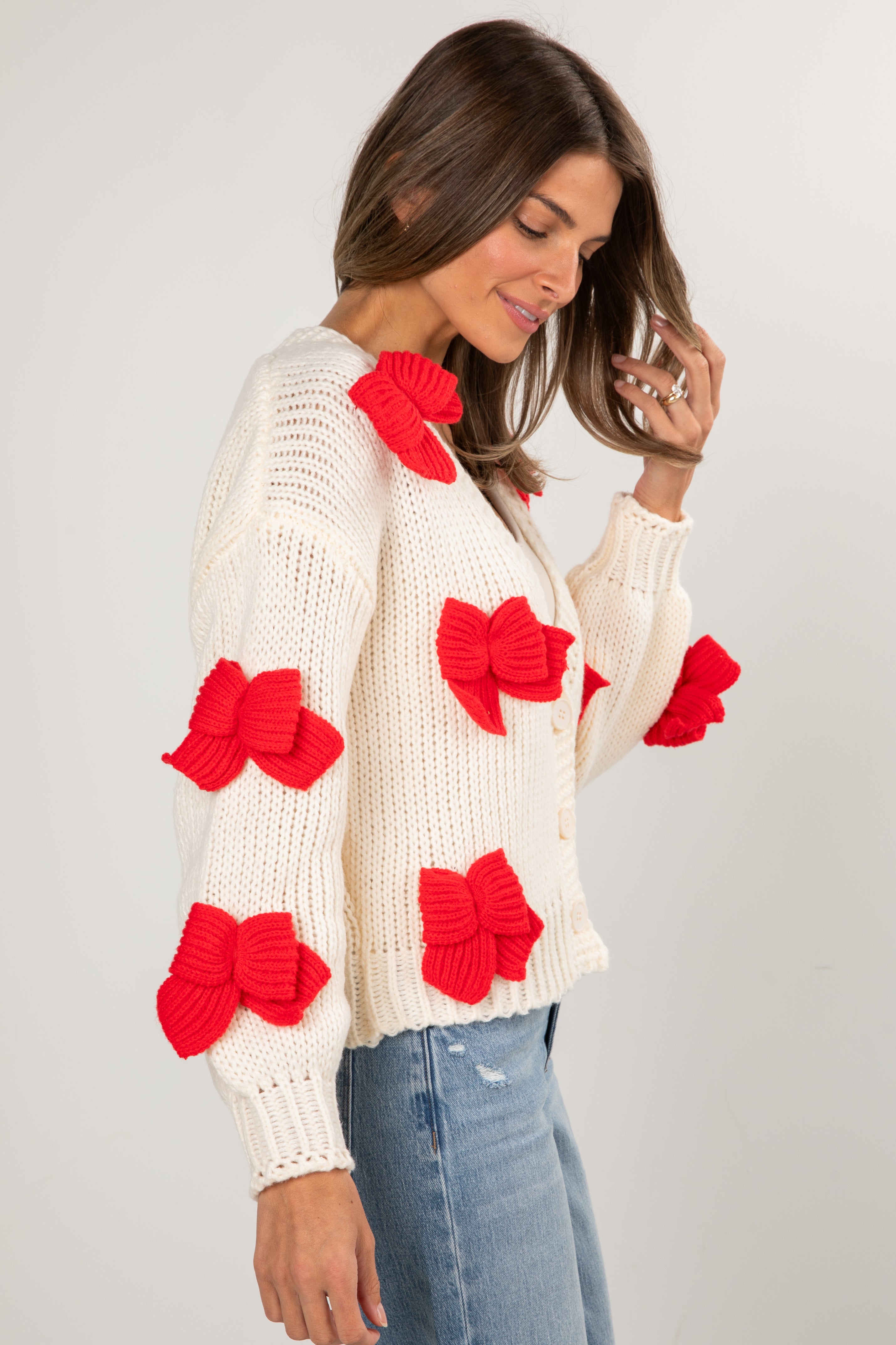 Woman wearing a white sweater with red bow patterns on a plain background