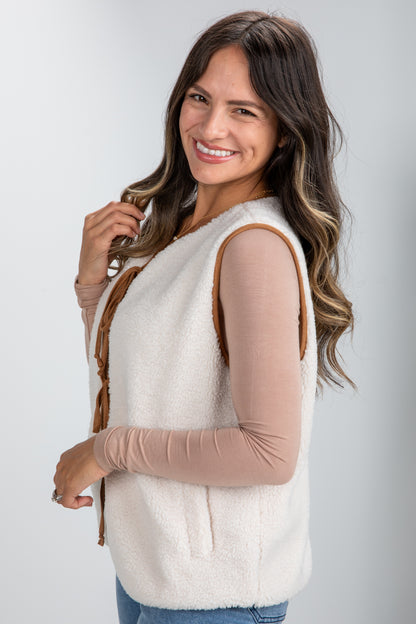 Woman wearing a white vest over a beige long-sleeve shirt on a plain background