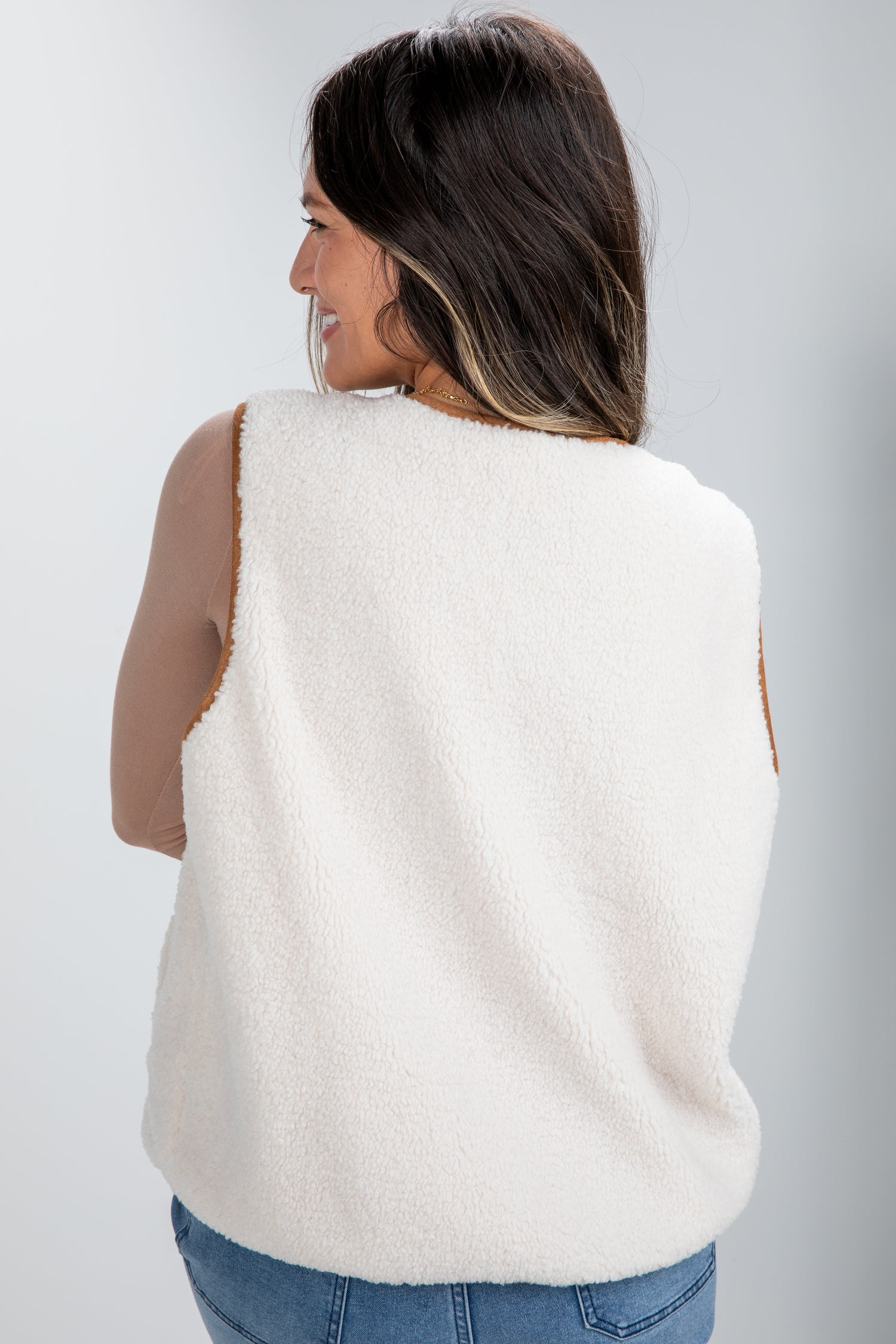 Woman wearing a white sleeveless sweater vest against a plain background