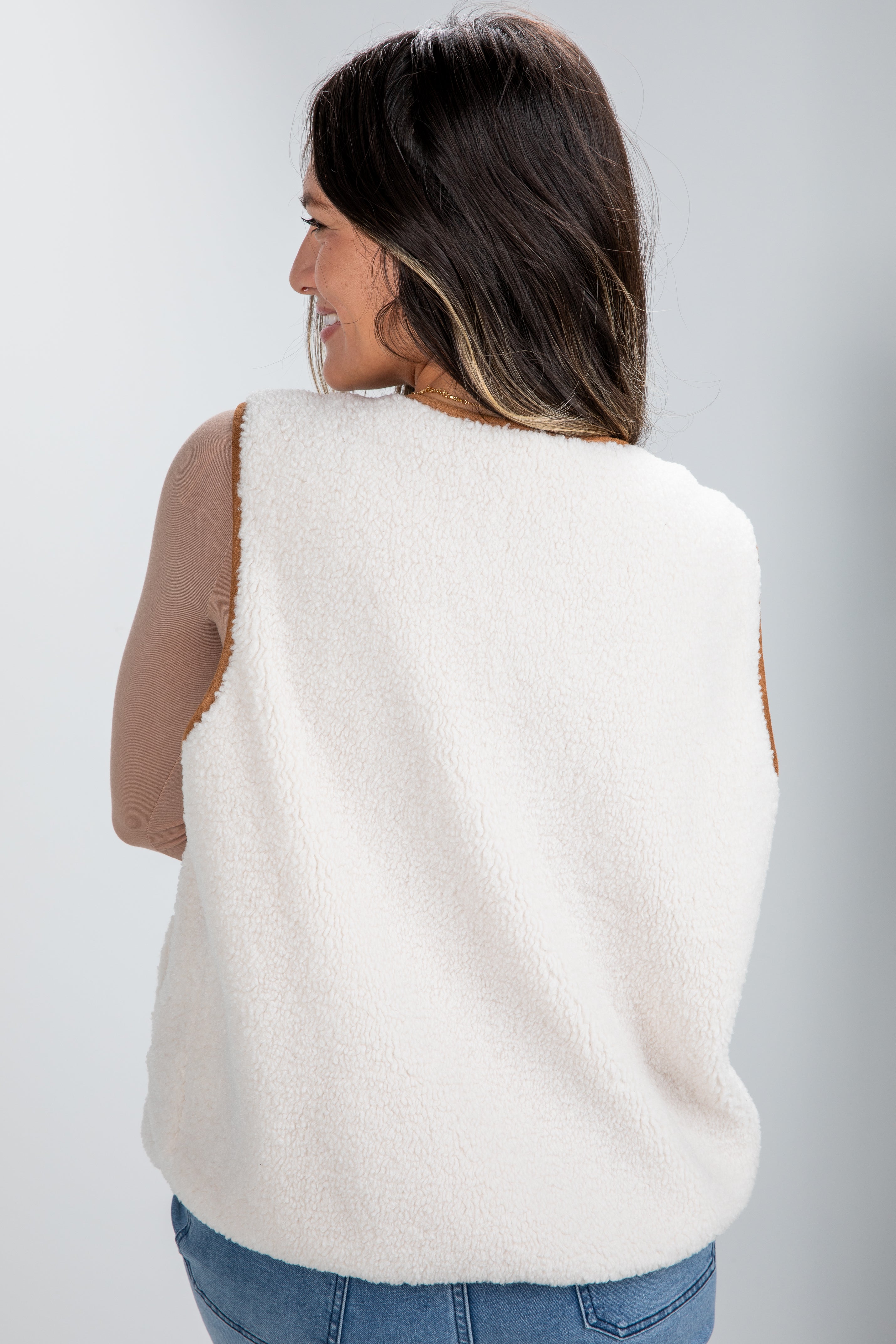 Woman wearing a white sleeveless sweater vest against a plain background