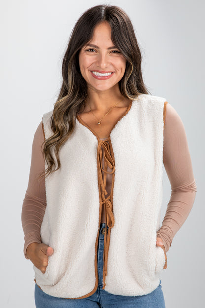 Woman wearing a cream-colored vest with a brown front panel on a light gray background