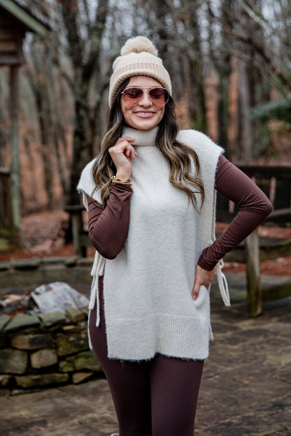 Woman wearing a white vest, brown long-sleeve top, and beige beanie outdoors.