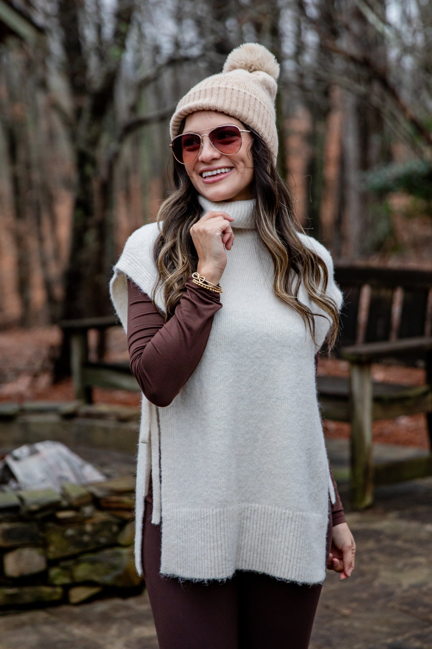 Woman wearing a white sweater vest and beige beanie in a forest setting