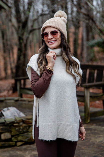 Woman wearing a white sweater vest and beige beanie in a forest setting