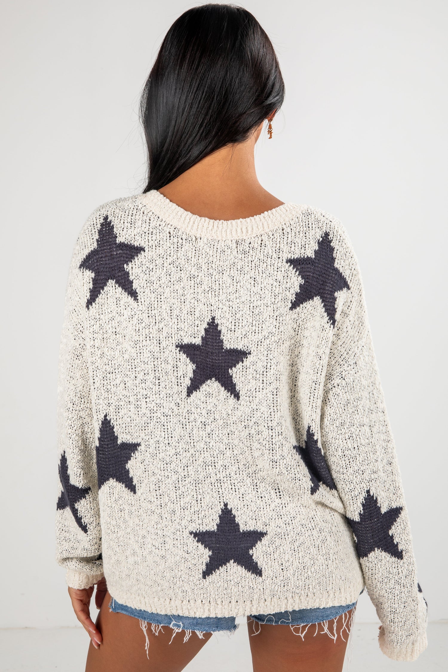 Person wearing a cream sweater with black star patterns on a white background