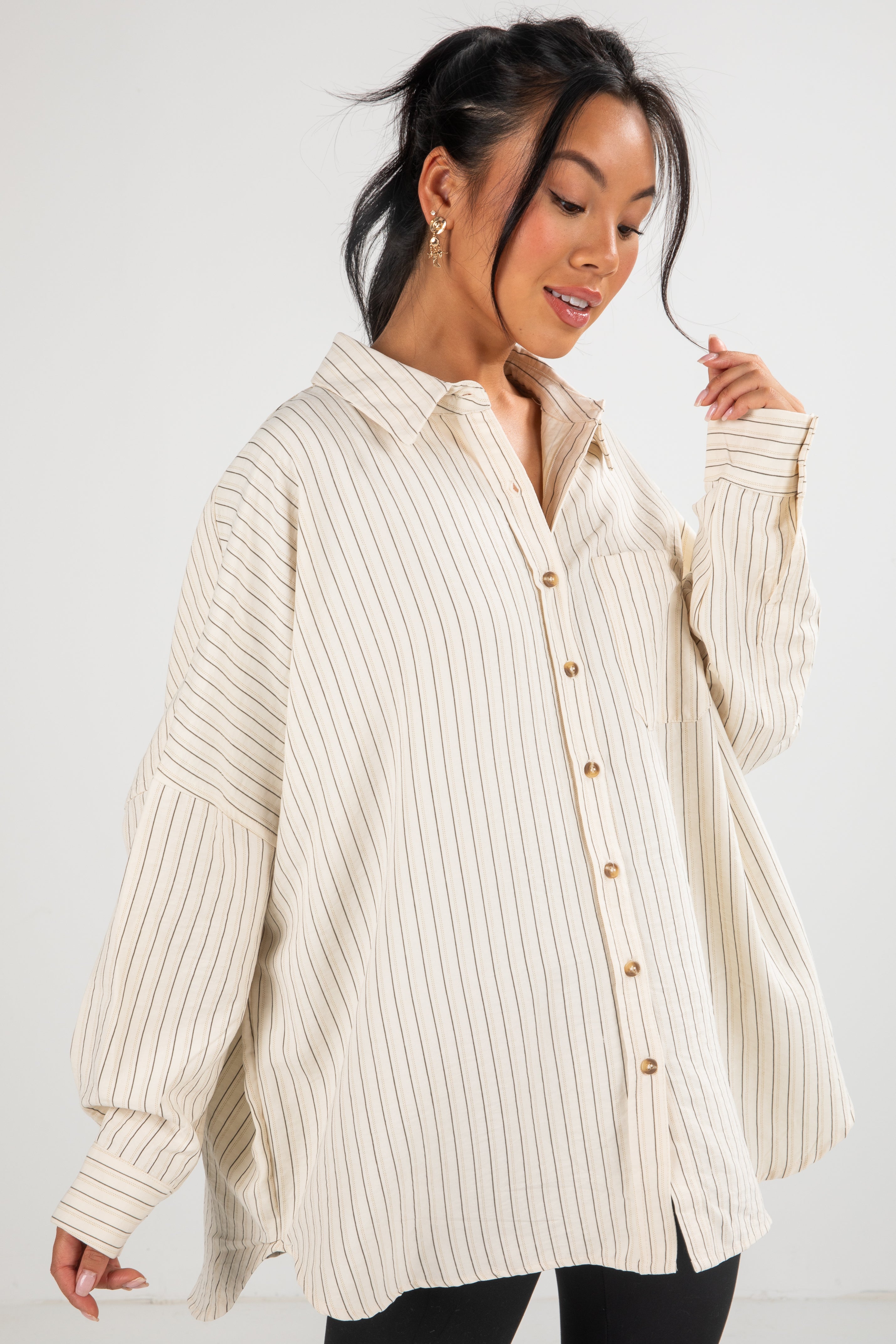 Woman wearing a cream ribbed sweater over a button-up shirt against a white background