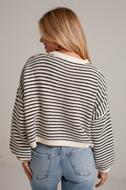 A woman shown from the back wearing a cropped knit sweater with thin horizontal black stripes on an off-white background, paired with light blue jeans.