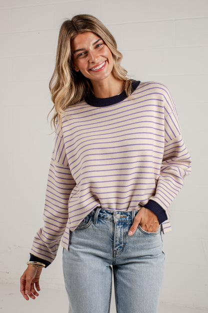 A woman wearing a light pink and navy blue horizontally striped long-sleeve knit top with dark navy ribbed collar, cuffs, and hem, paired with light-wash blue jeans.