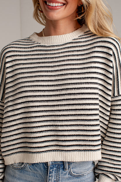 A close-up of a woman wearing a black and off-white horizontally striped knit sweater with blue jeans.
