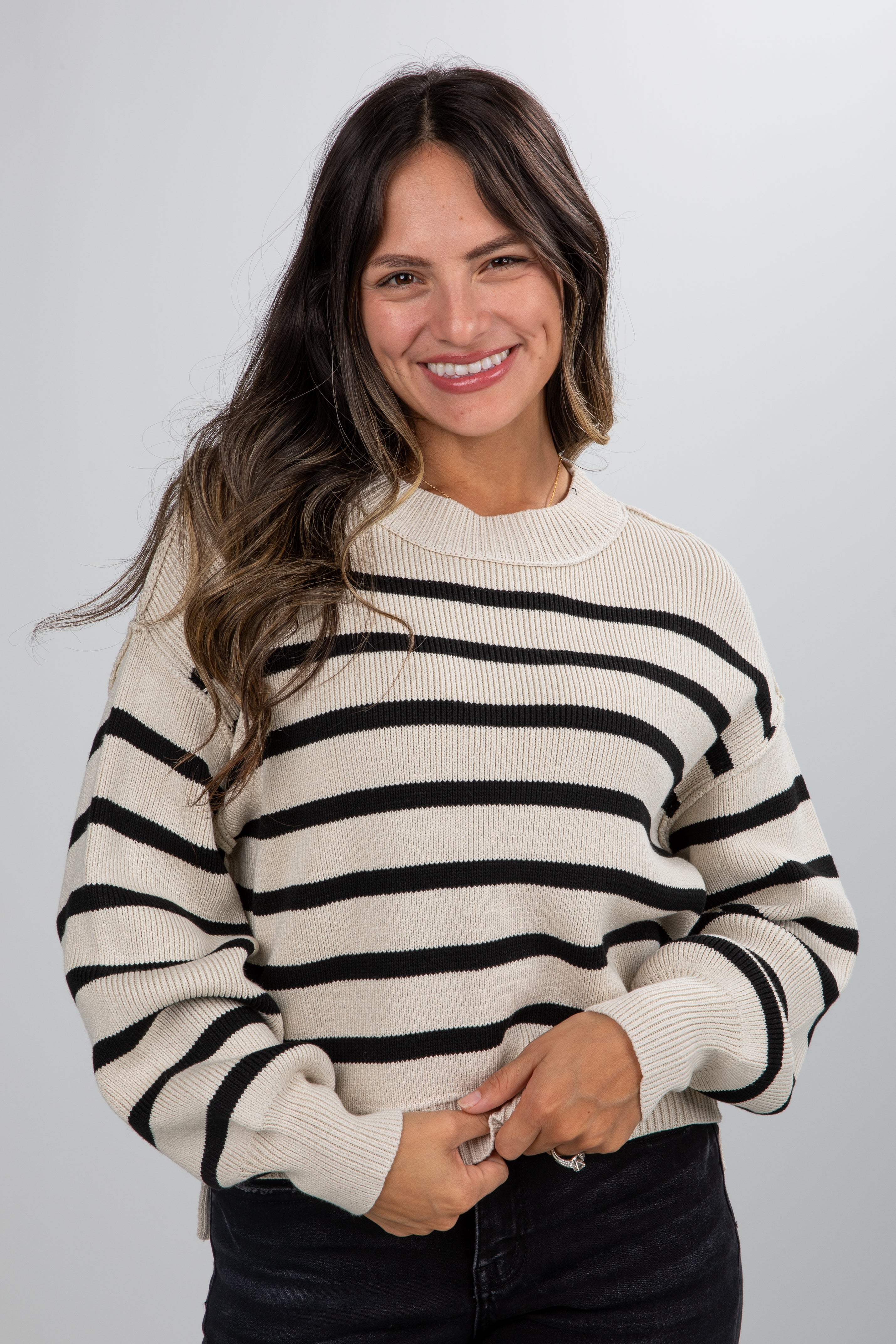 Woman wearing a cream and black striped sweater against a plain background