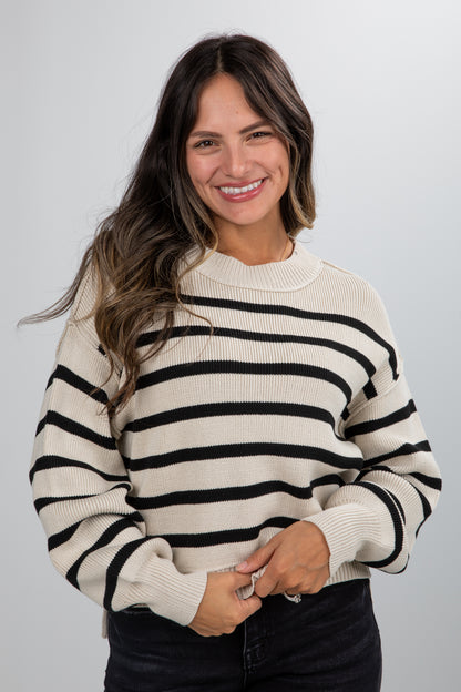 Woman wearing a cream and black striped sweater against a plain background