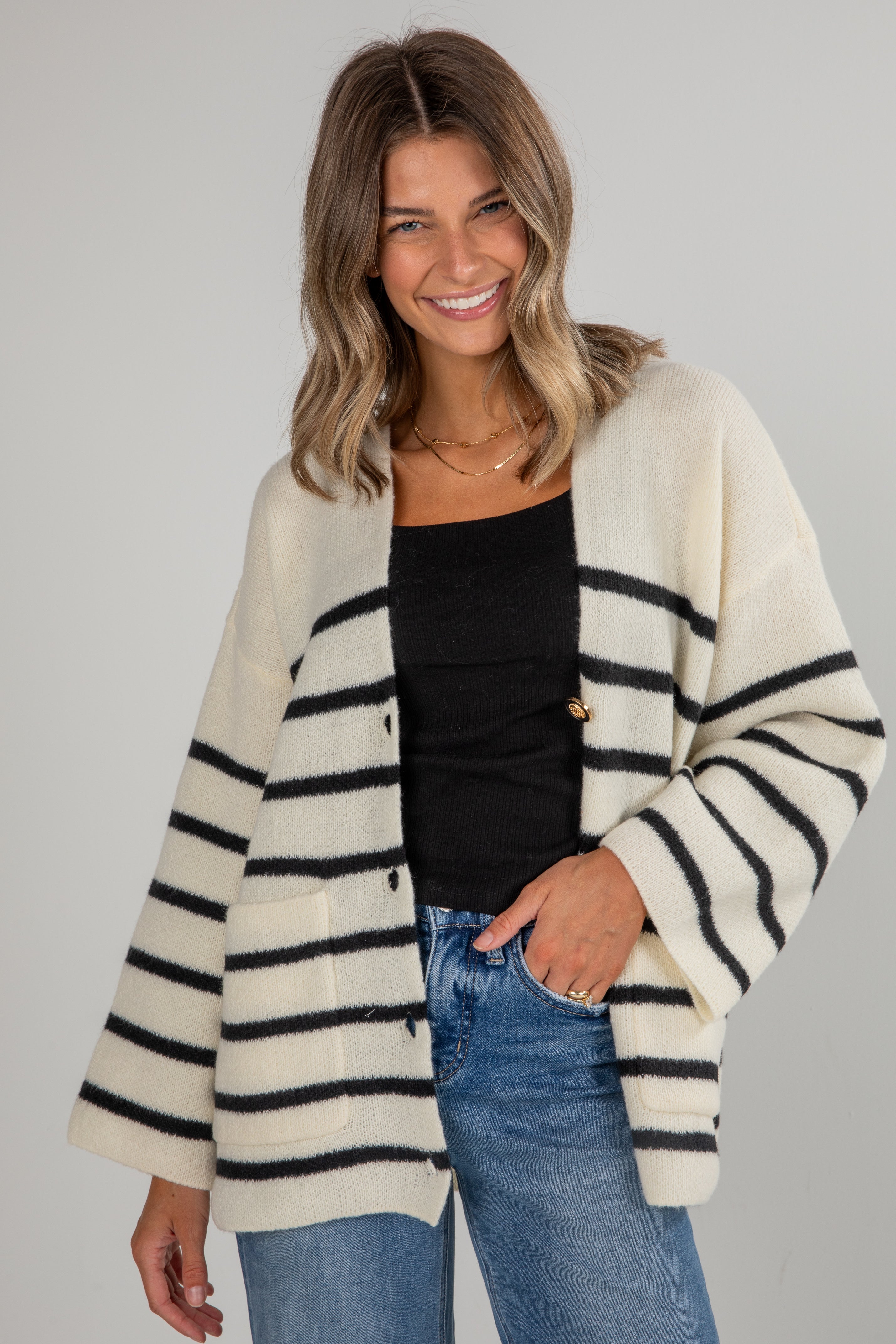 Woman wearing a cream and navy striped cardigan with a plain background