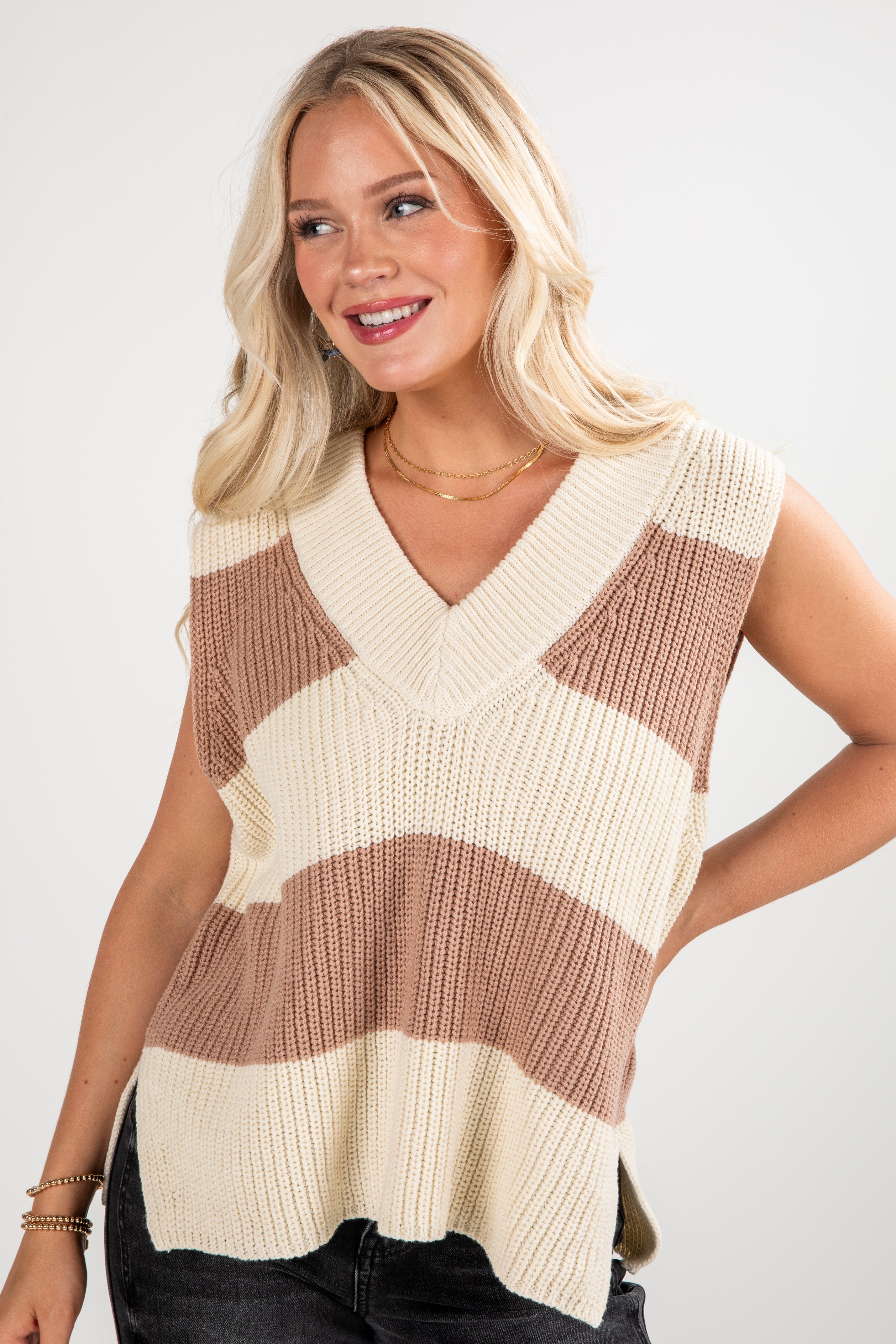 Woman wearing a sleeveless striped sweater vest against a plain background