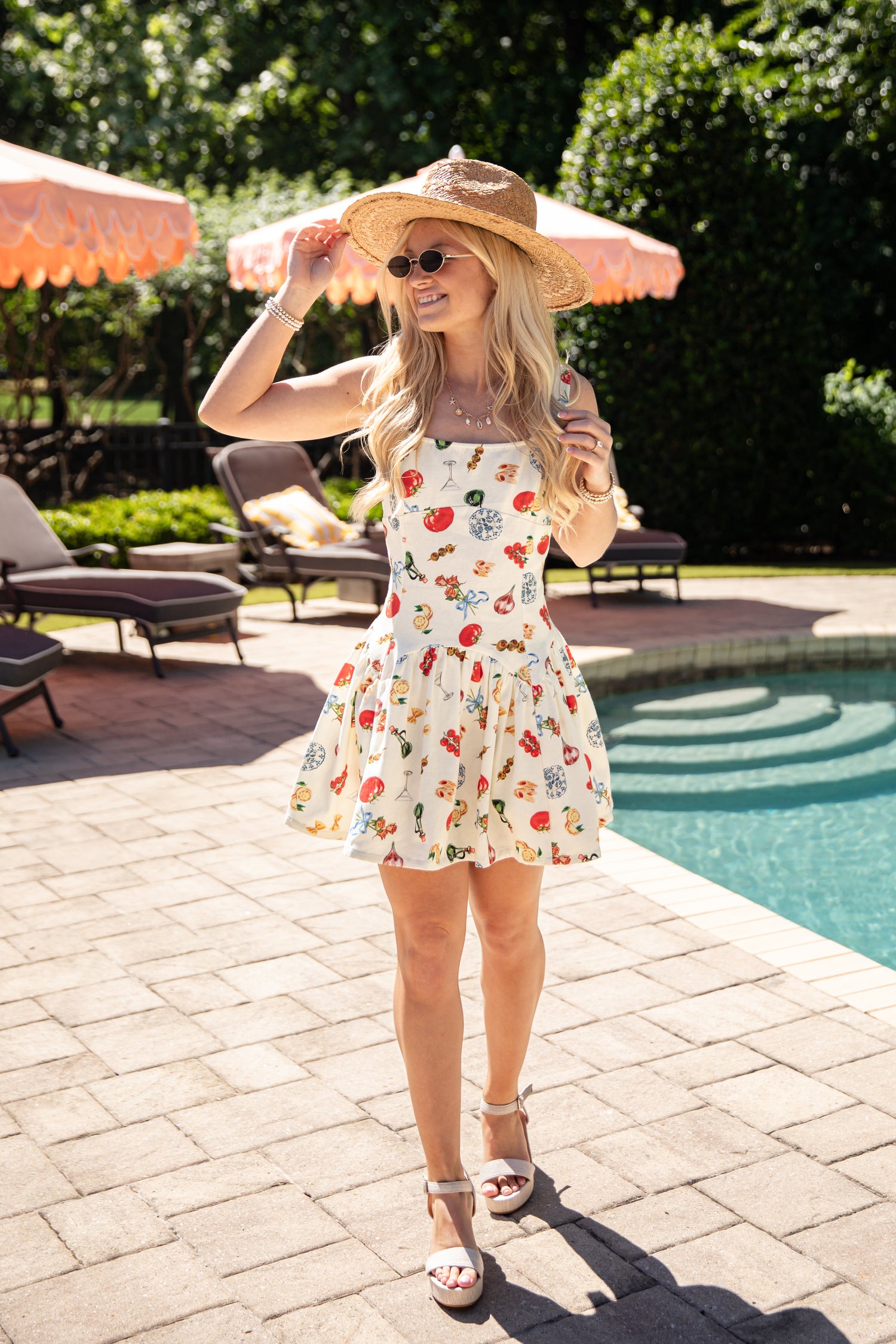 Woman in a patterned dress and sun hat by a poolside