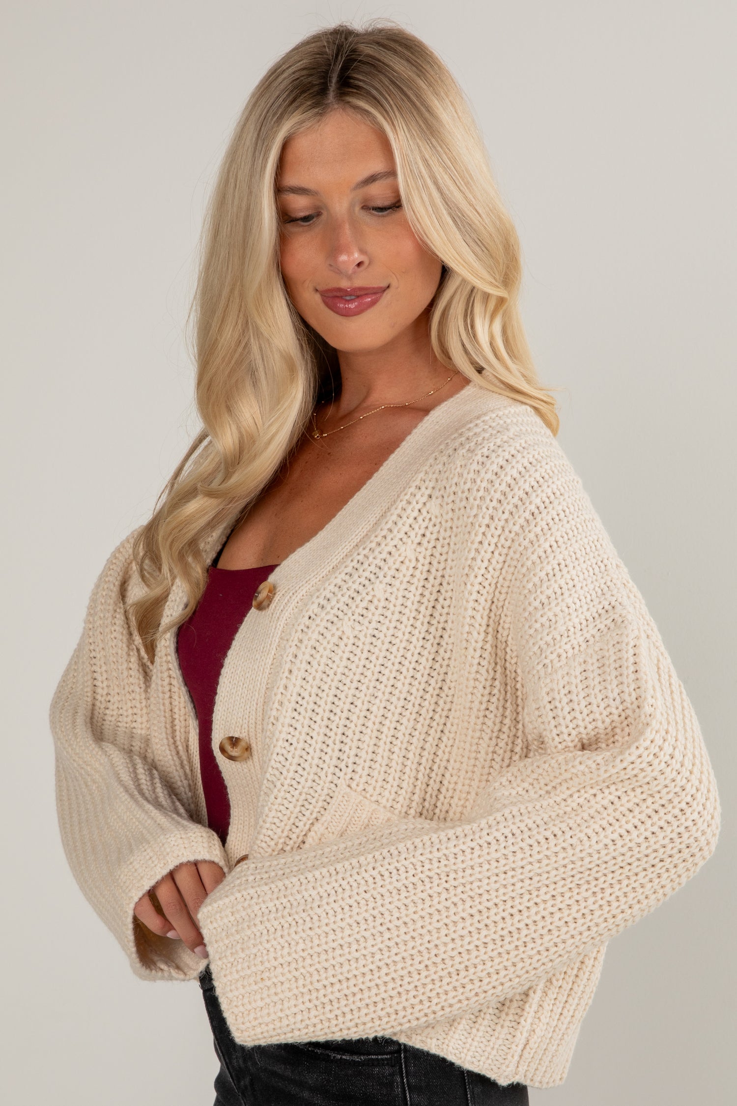 Woman wearing a beige knitted cardigan on a plain background