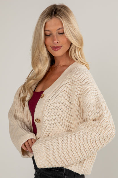 Woman wearing a beige knitted cardigan on a plain background